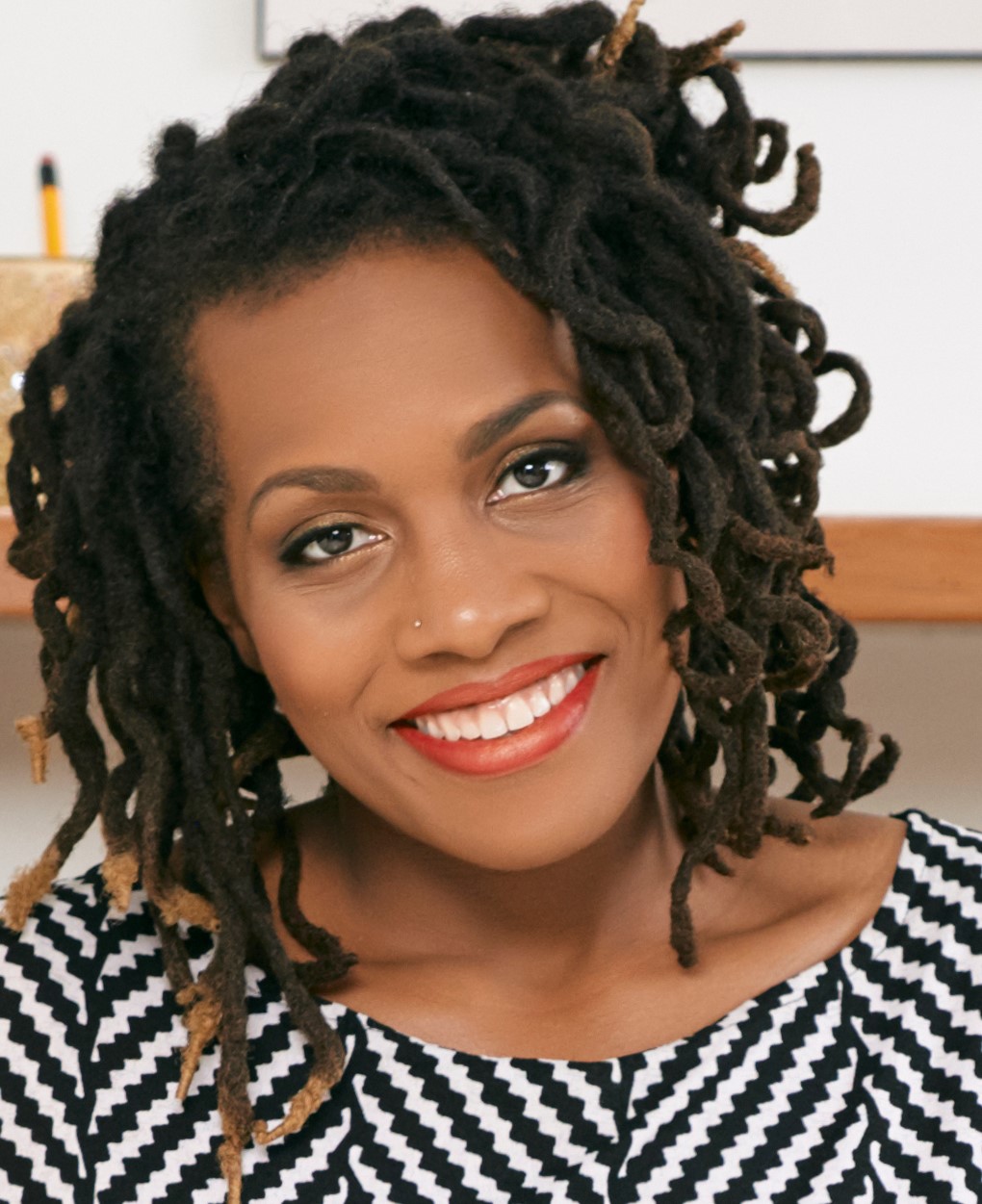 Portrait of young black business lady in beautiful dress sitting on office desk and smiling